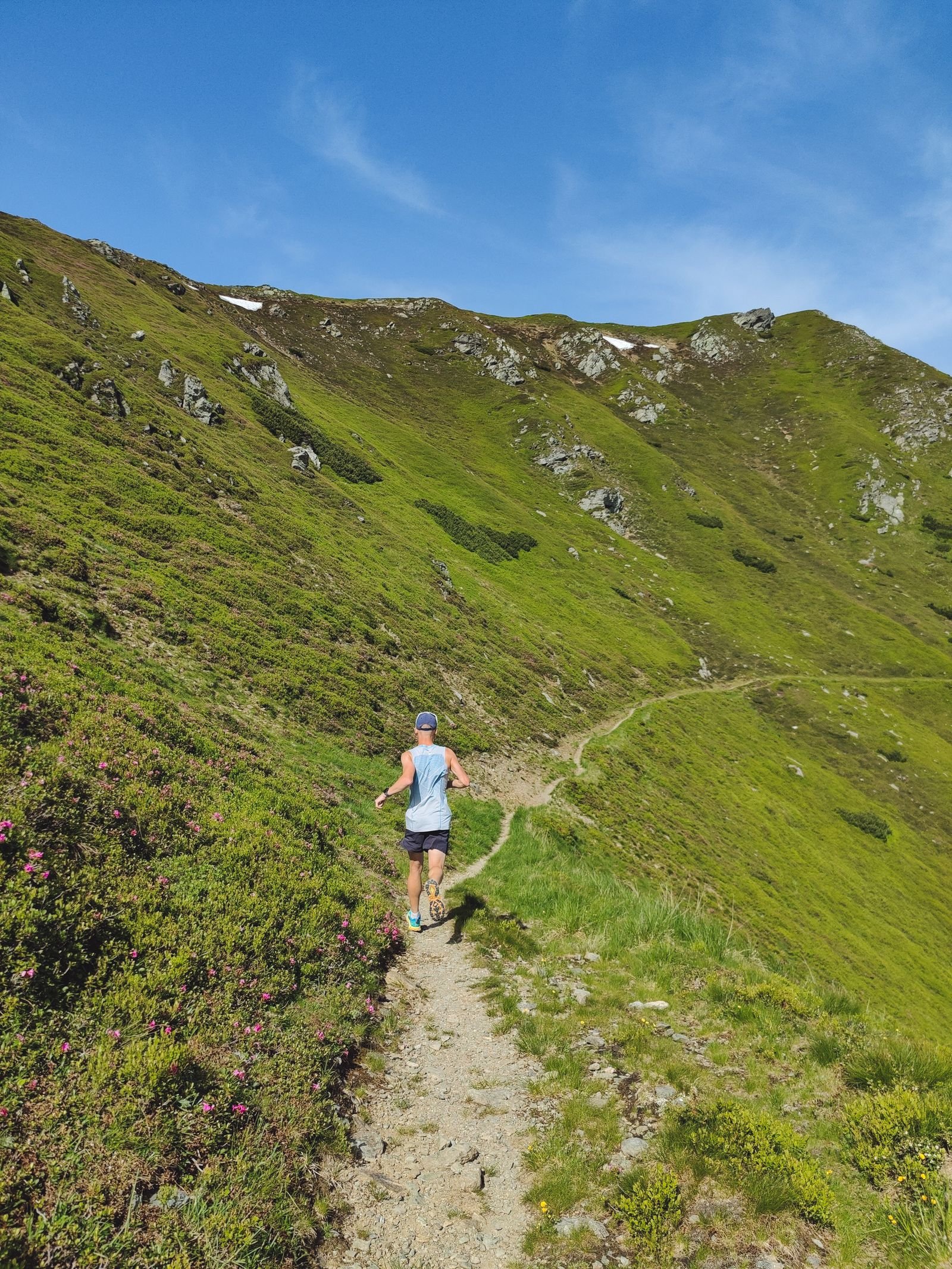 A runner following a narrow stony path across a steep fellside, shown in a dusky night-time tint